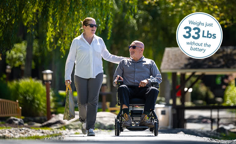 A man using a Jazzy Ultra Light on a park path with a companion